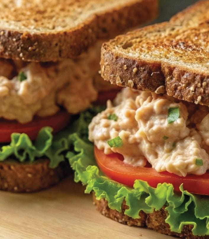 A fish sandwich on a plate with tomato and lettuce.