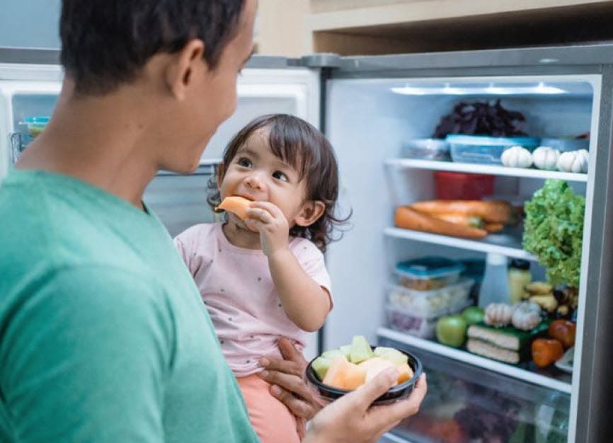 A man holding a little girl while they eat melon